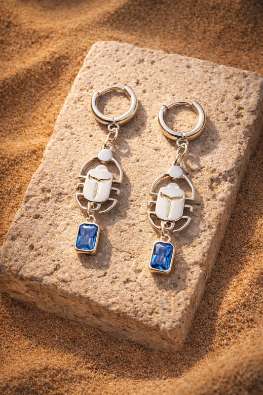 Sterling silver scarab earrings with blue stones on sand and stone
