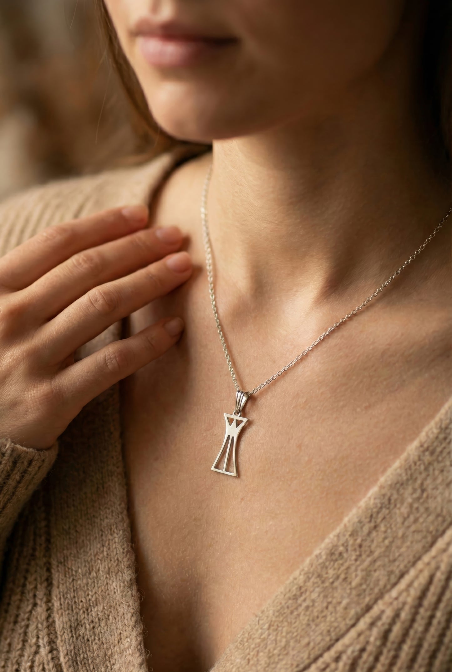 Close-up of a woman wearing a silver necklace with a lotus column pendant, blurred background