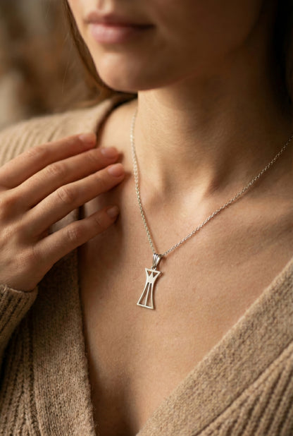 Close-up of a woman wearing a silver necklace with a lotus column pendant, blurred background