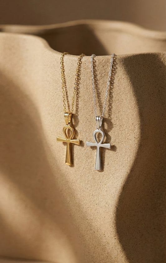 Two ankh necklaces, one gold and one silver, on a beige surface.