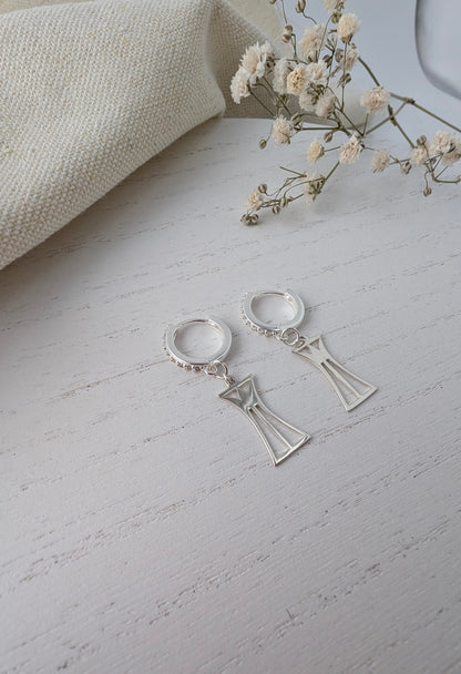 Silver lotus column earrings on a light gray surface with a beige fabric and small flowers in the background.