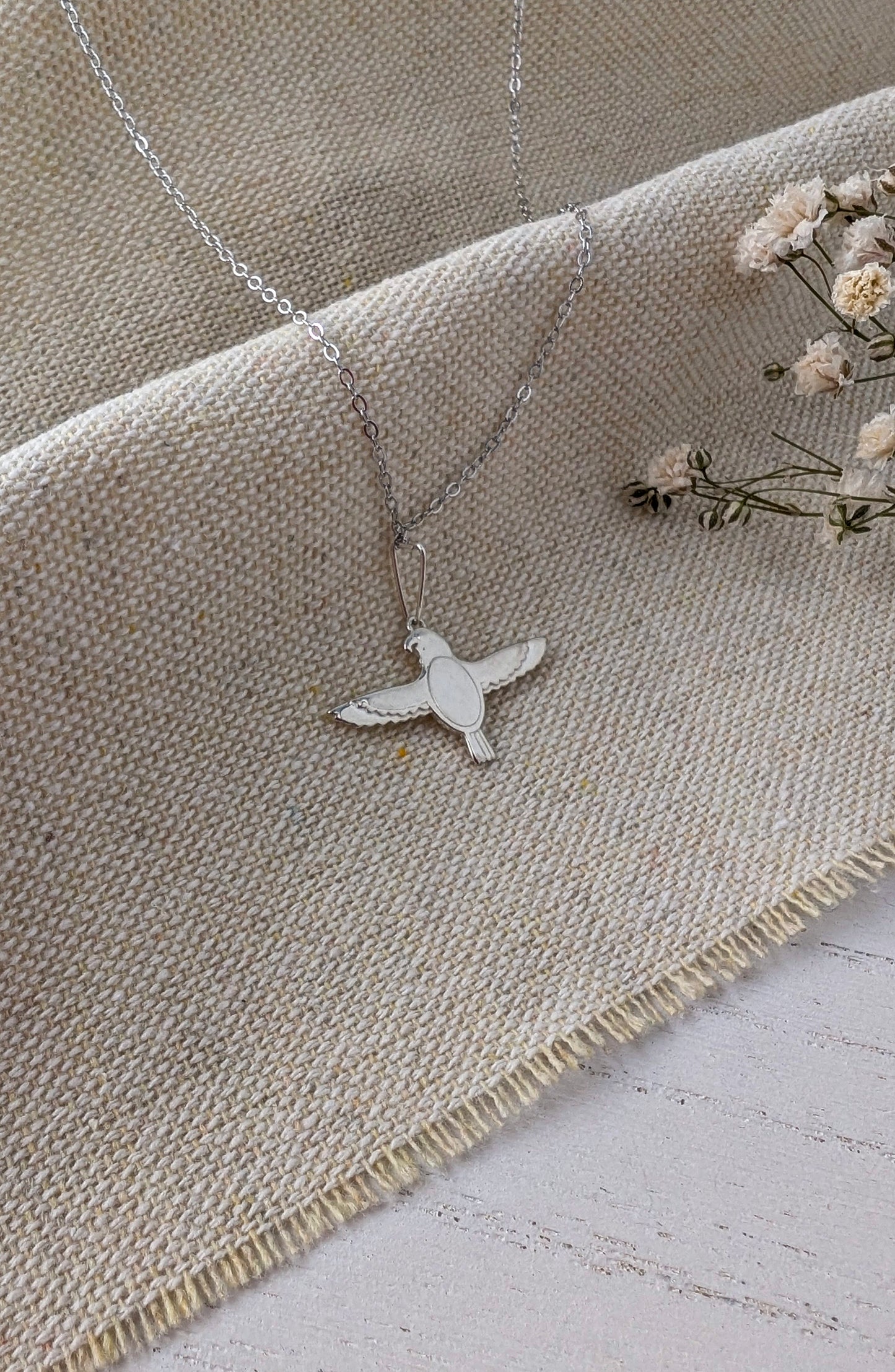 silver falcon necklace on beige linen surface