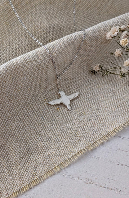 silver falcon necklace on beige linen surface