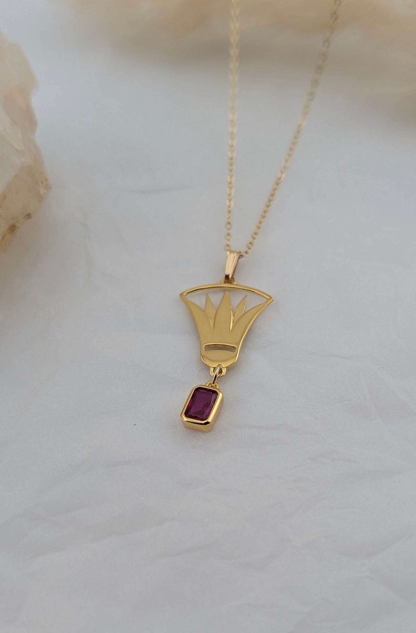 Gold necklace with a lotus pendant featuring a red gemstone on a light background