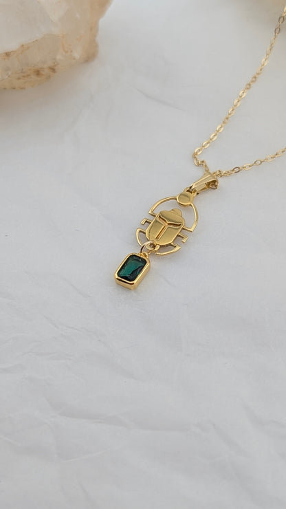Gold necklace with a green gemstone scarab pendant on a light background