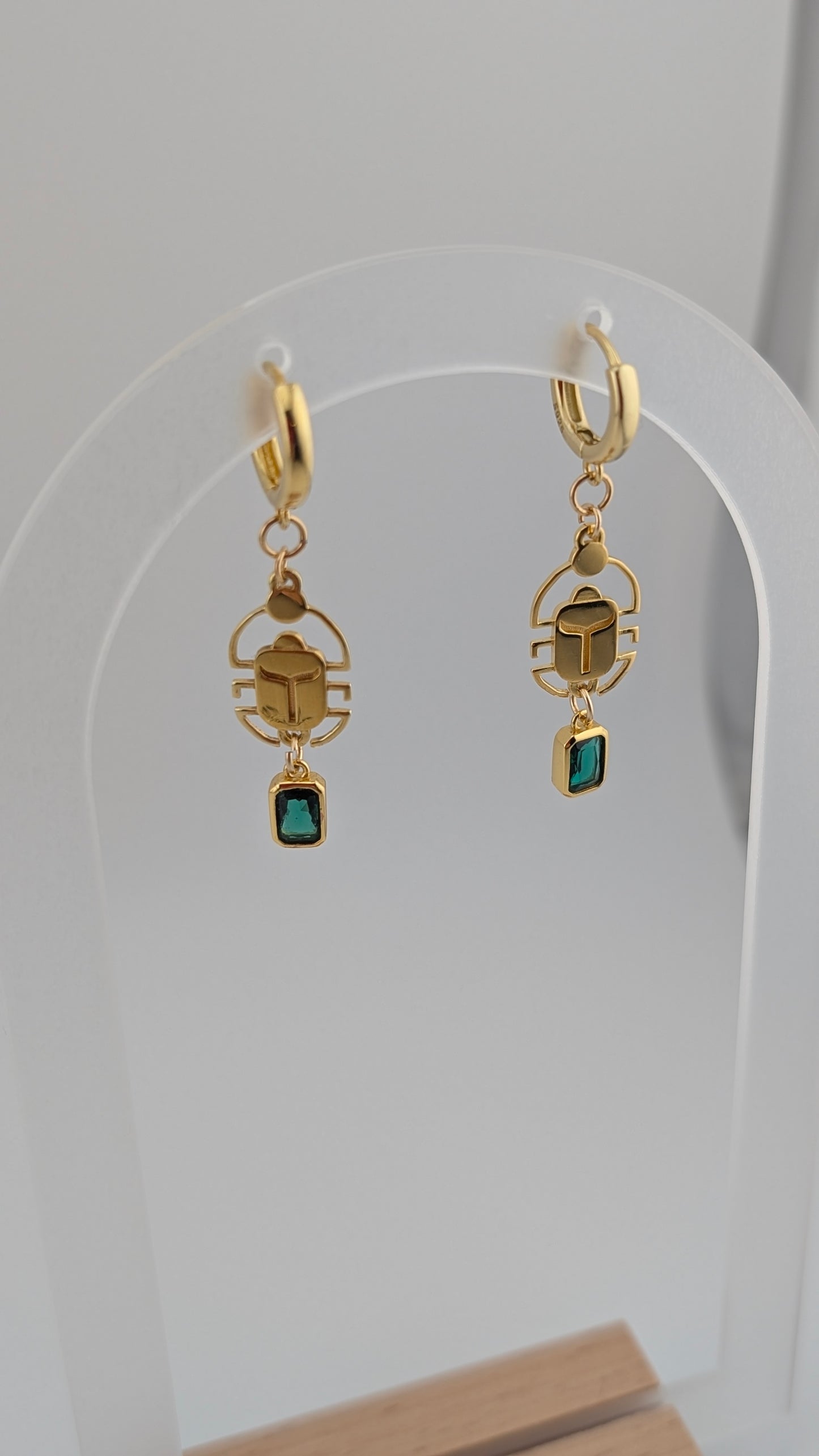 Gold scarab earrings with green gemstones on a white background