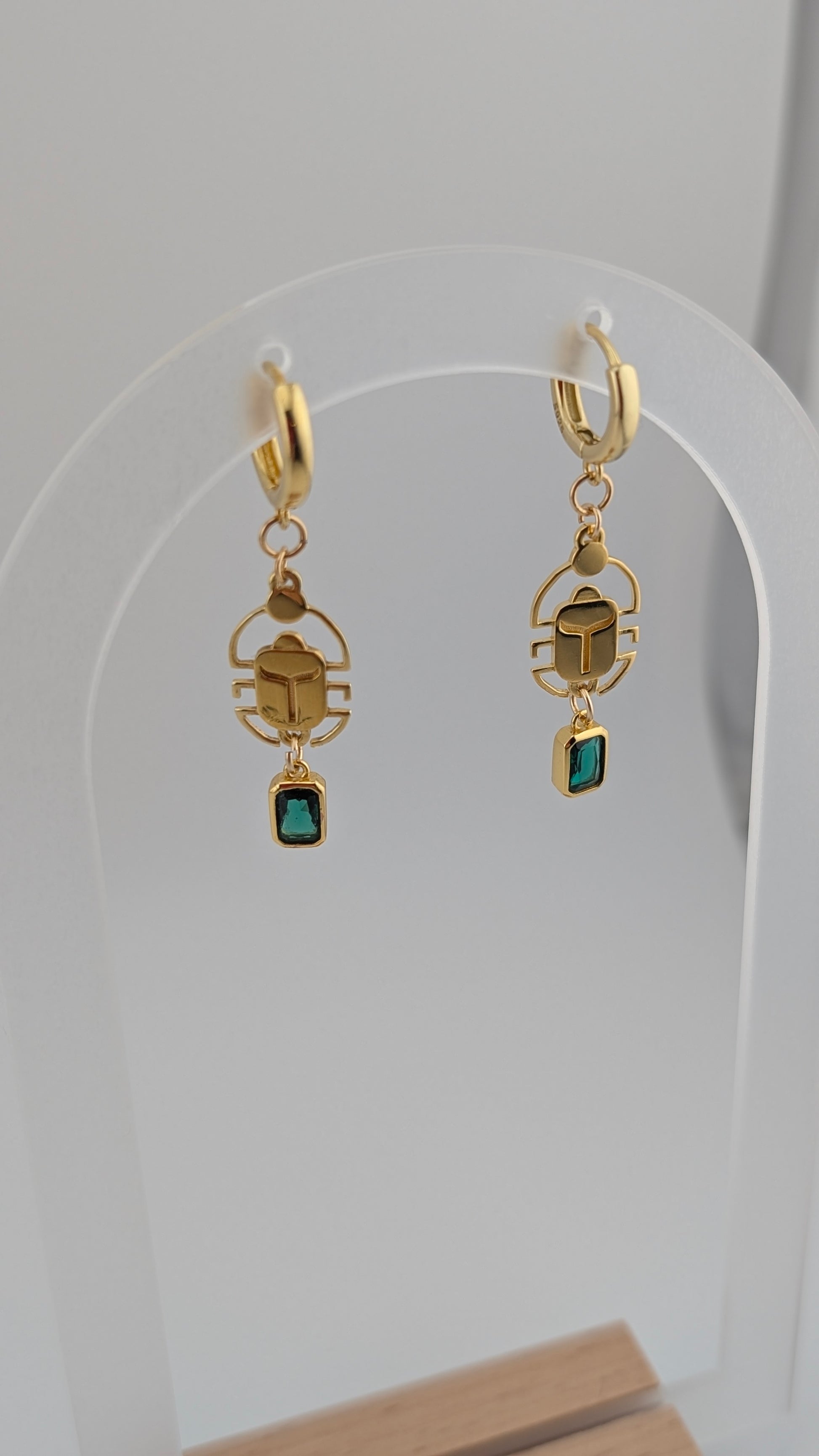 Gold scarab earrings with green gemstones on a white background