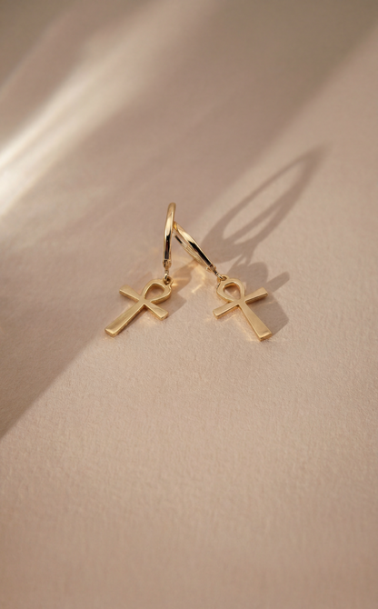 Gold ankh earrings on a beige background