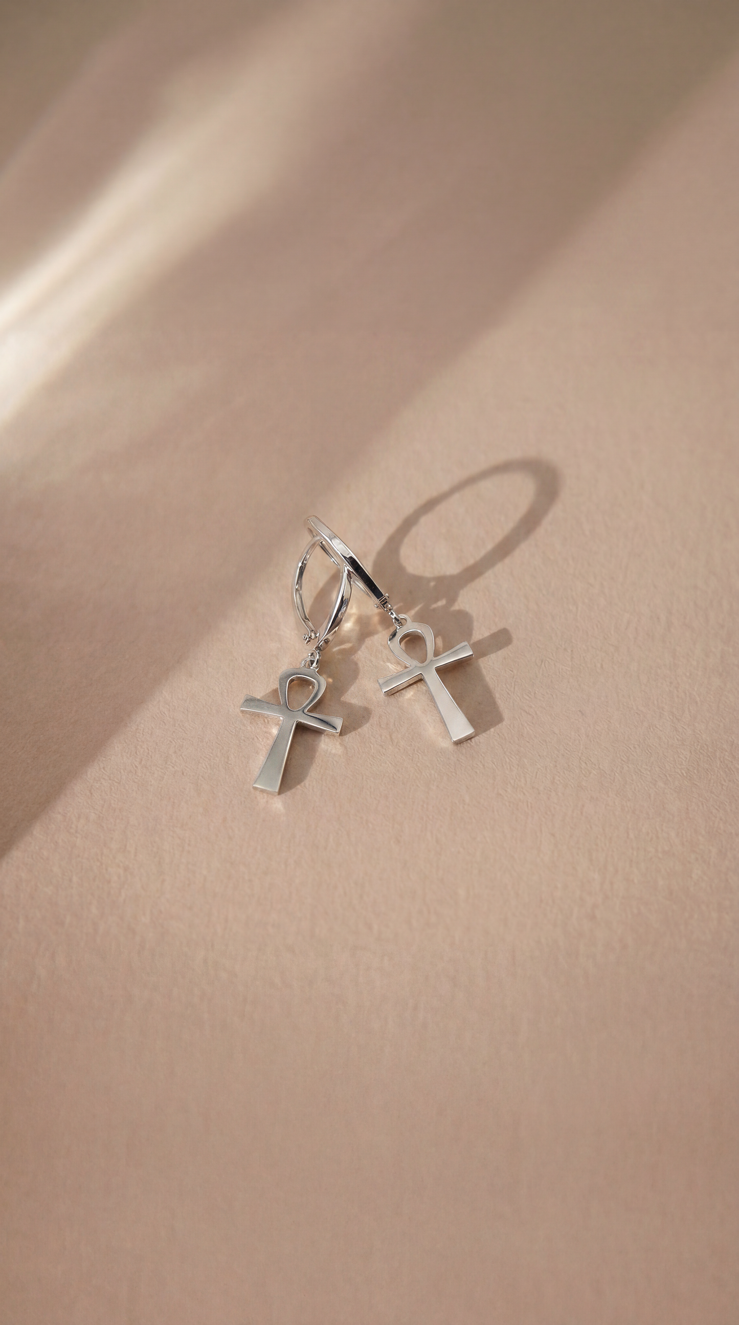Silver ankh earrings on a beige surface