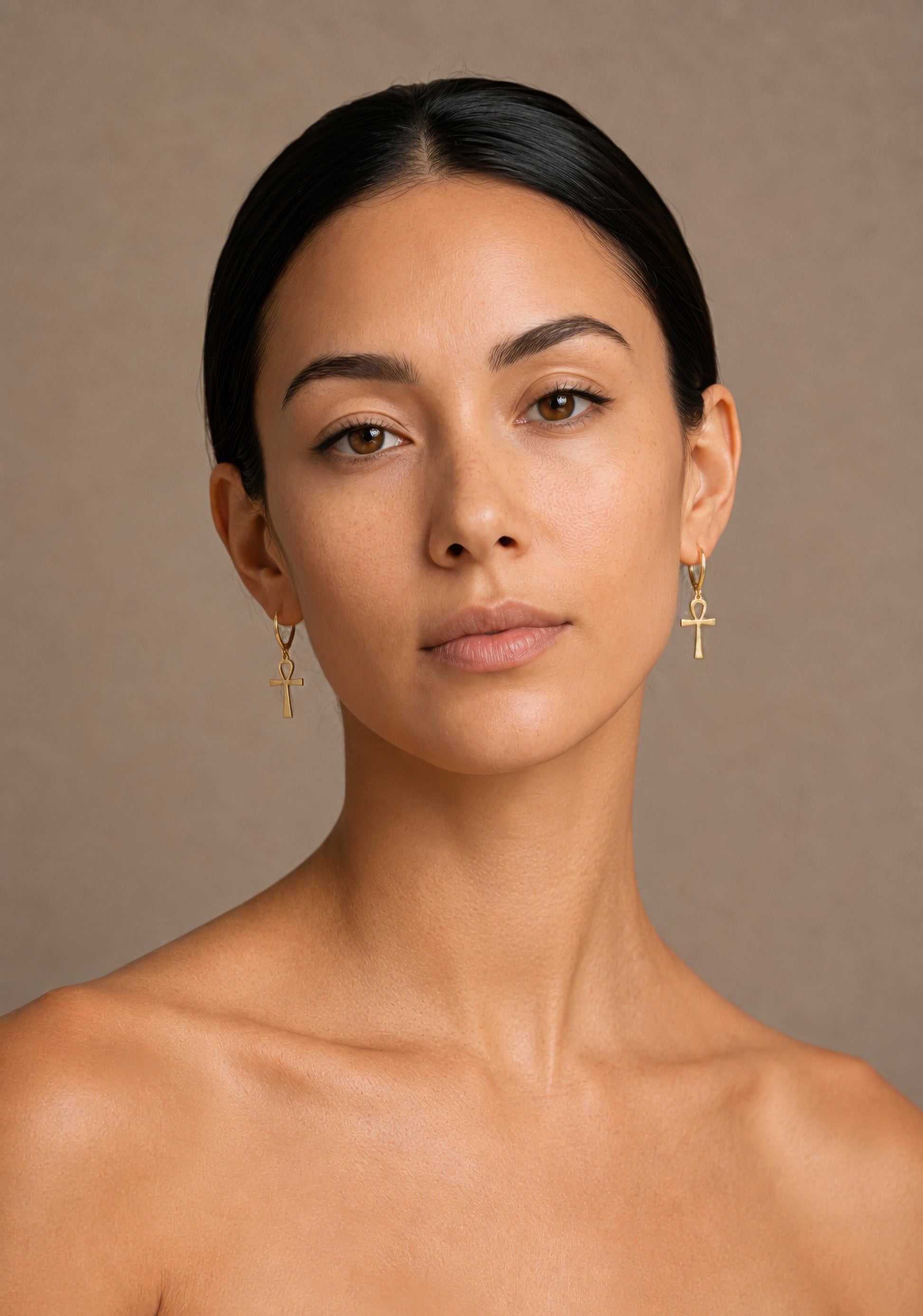 Woman wearing gold ankh earrings against a beige background