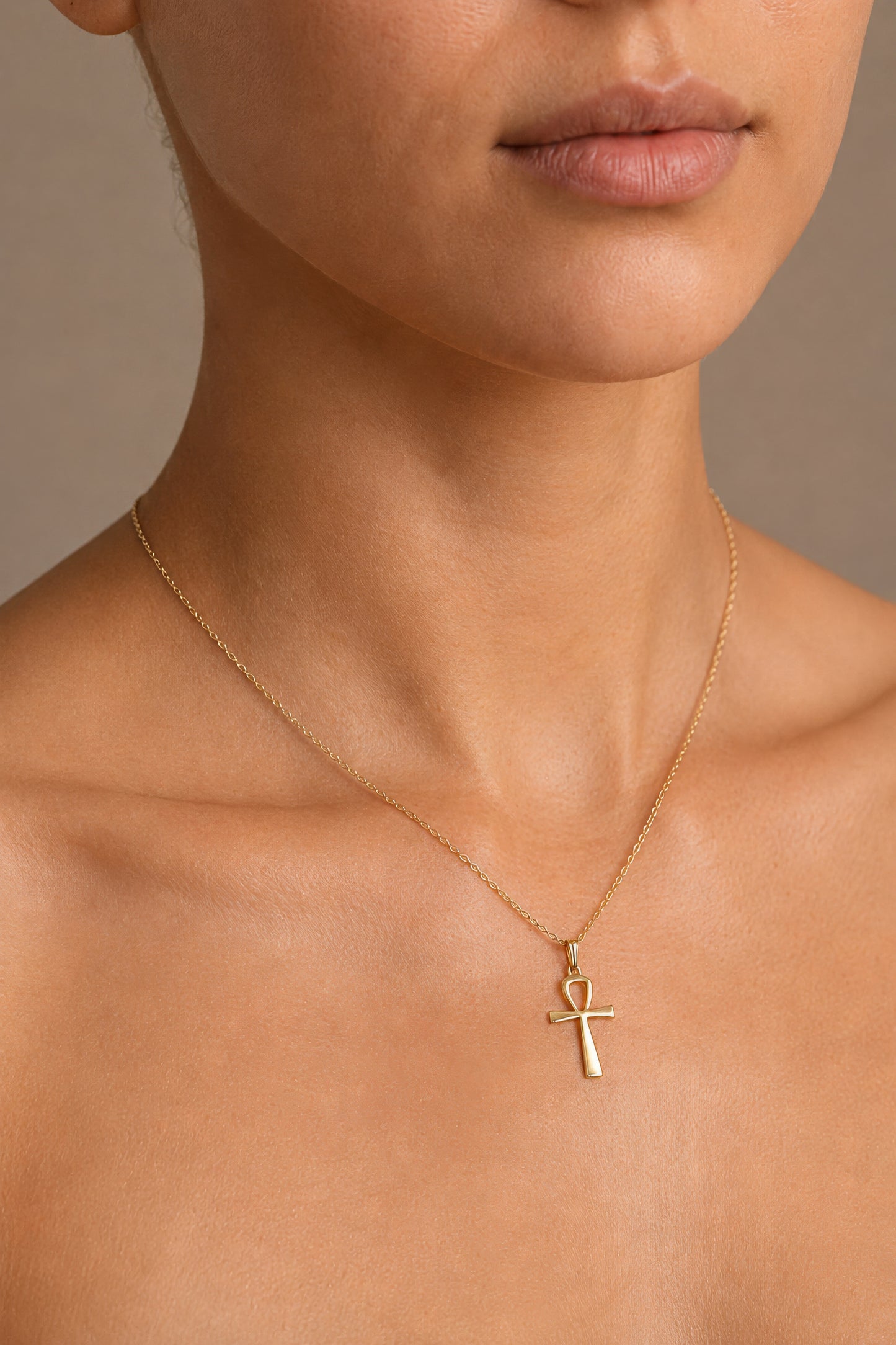 Close-up of a woman wearing a gold necklace with an ankh pendant on a neutral background