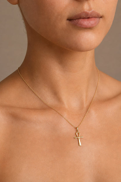 Close-up of a woman wearing a gold necklace with an ankh pendant on a neutral background