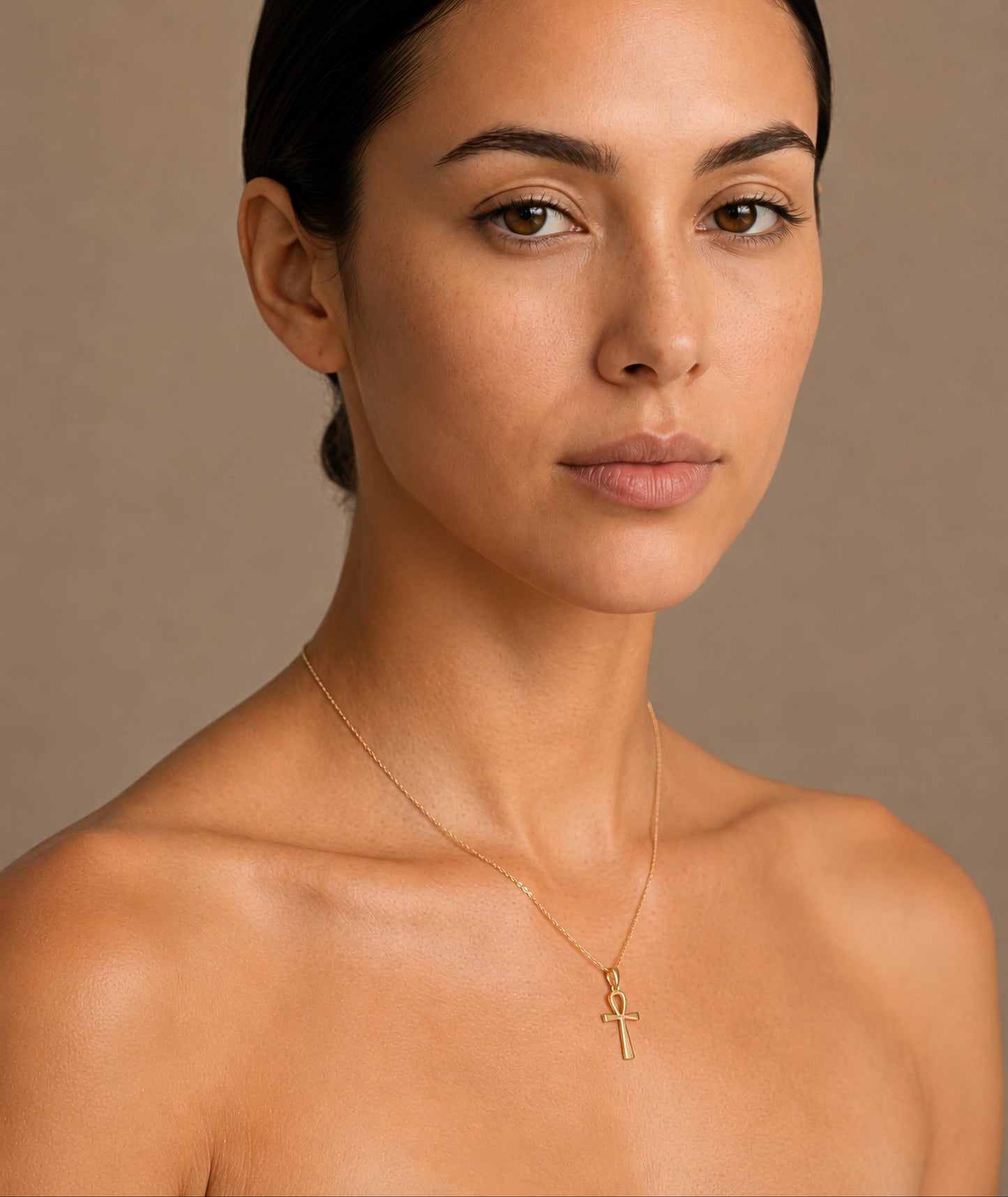 Woman wearing a gold necklace with ankh pendant against a beige background