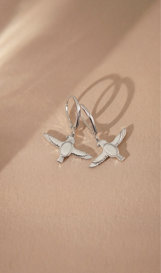 Silver falcon-shaped earrings on a beige background