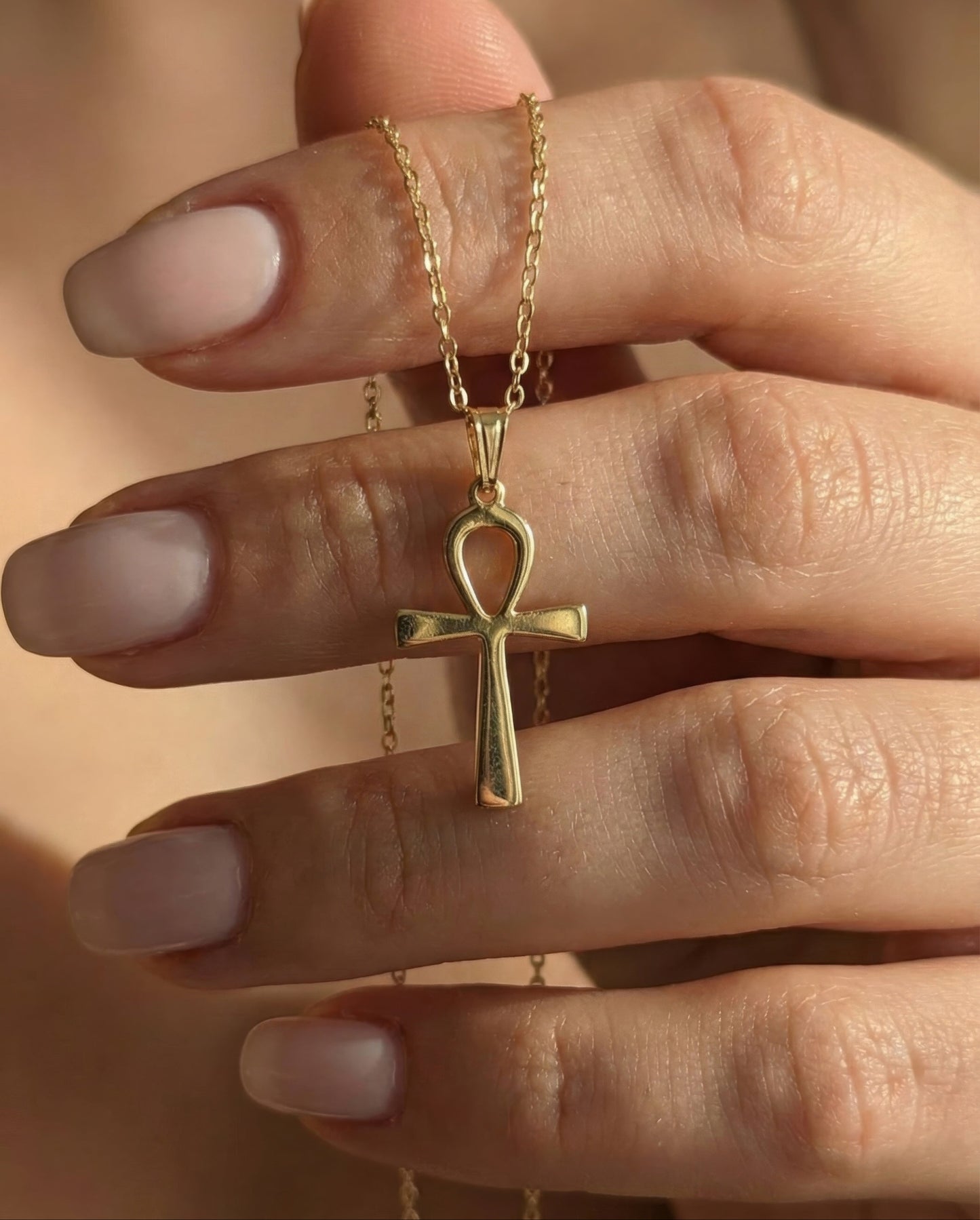 Gold necklace with an ankh pendant held by a hand