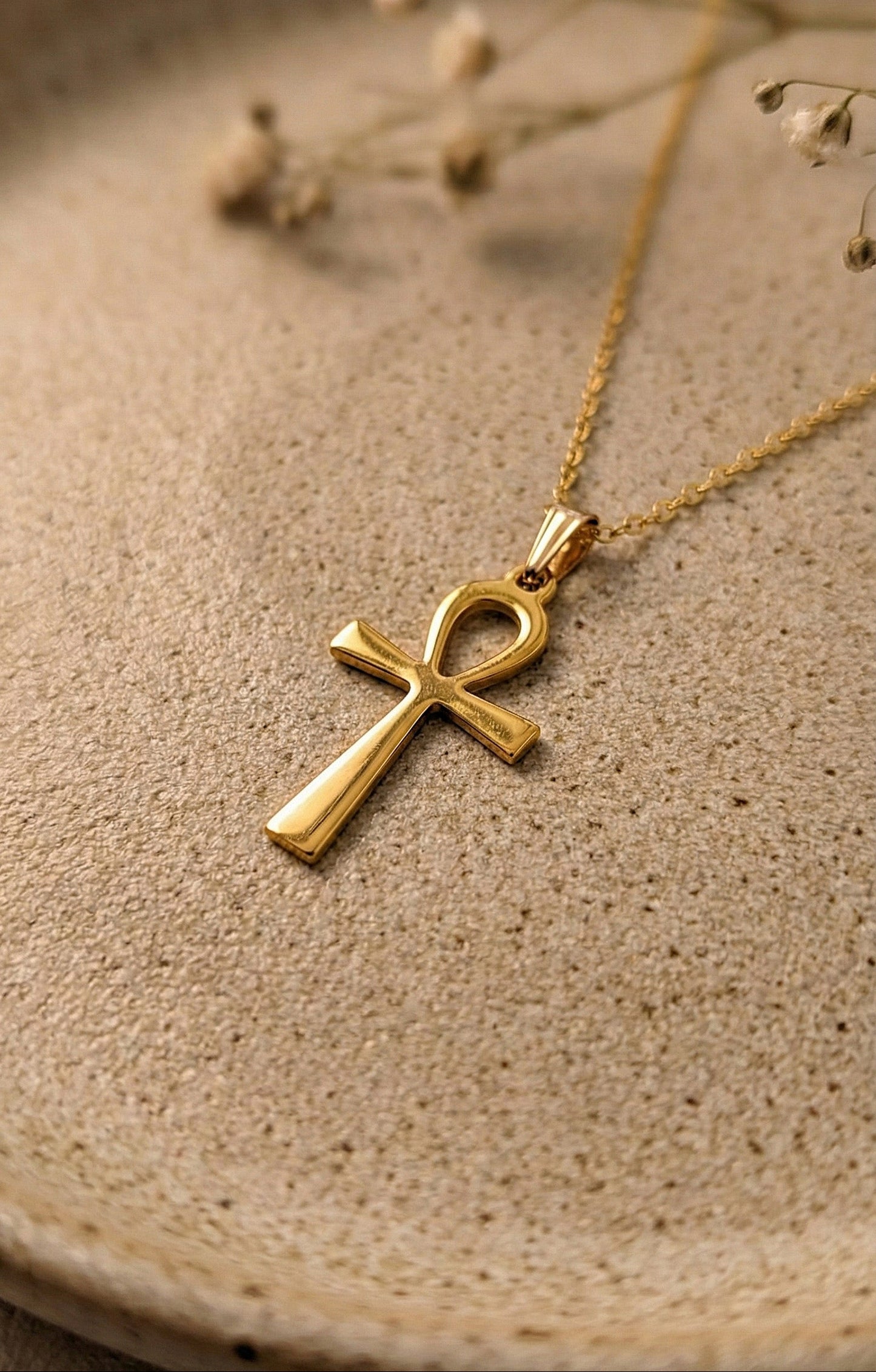 Gold Ankh pendant necklace on a ceramic beige surface