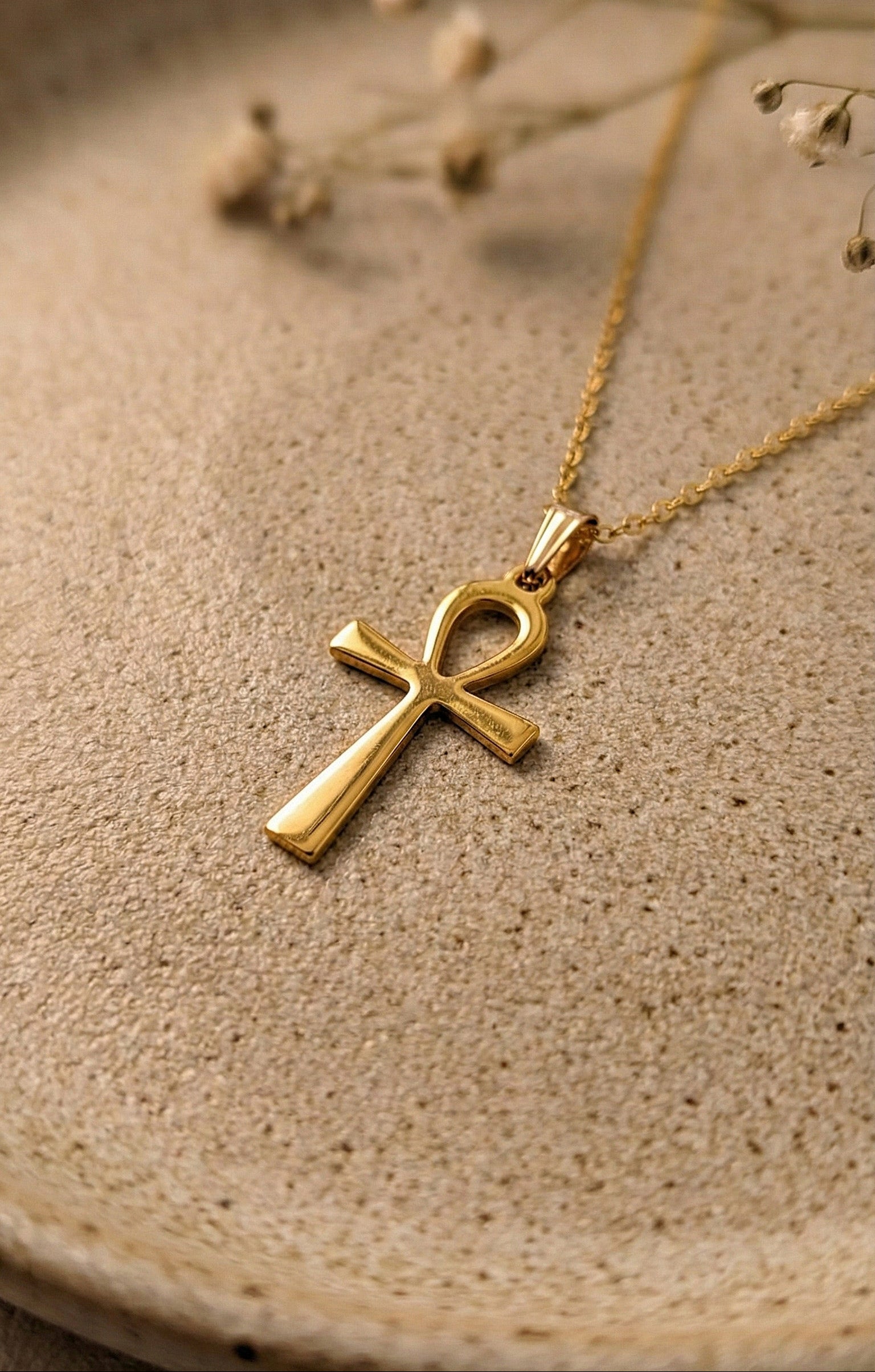Gold Ankh pendant necklace on a ceramic beige surface