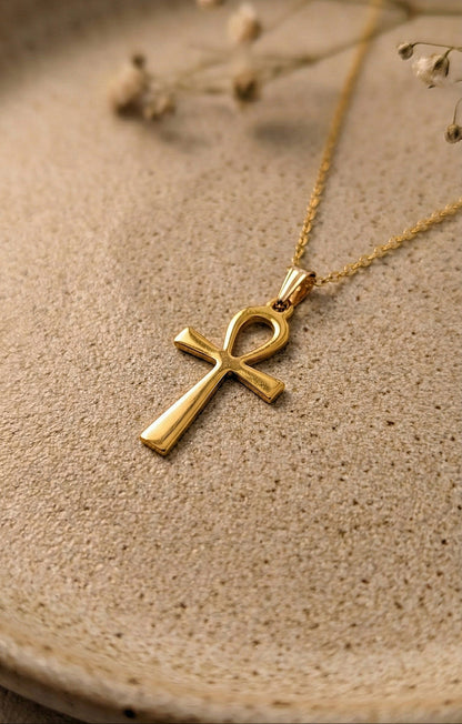 Gold Ankh pendant necklace on a ceramic beige surface