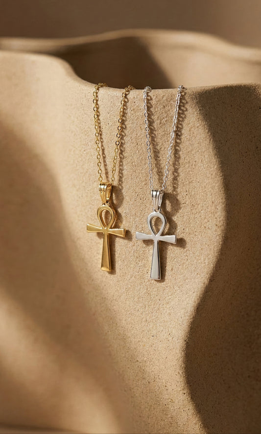 Gold and silver ankh necklaces on warm stone background