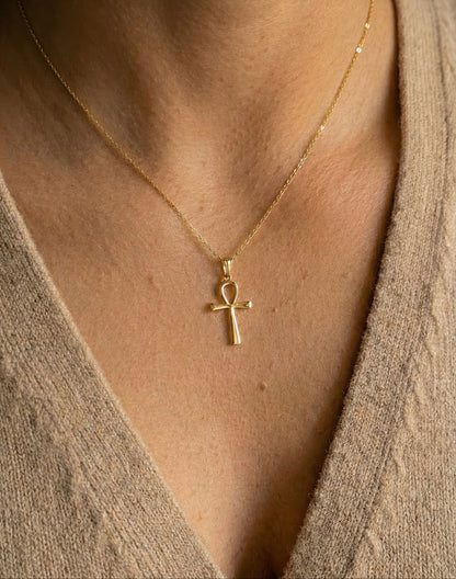 Gold necklace with ankh pendant worn by a person in a beige sweater.