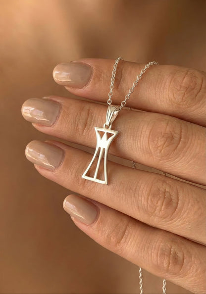 Silver lotus column pendant necklace held by a hand with beige nail polish against a blurred background