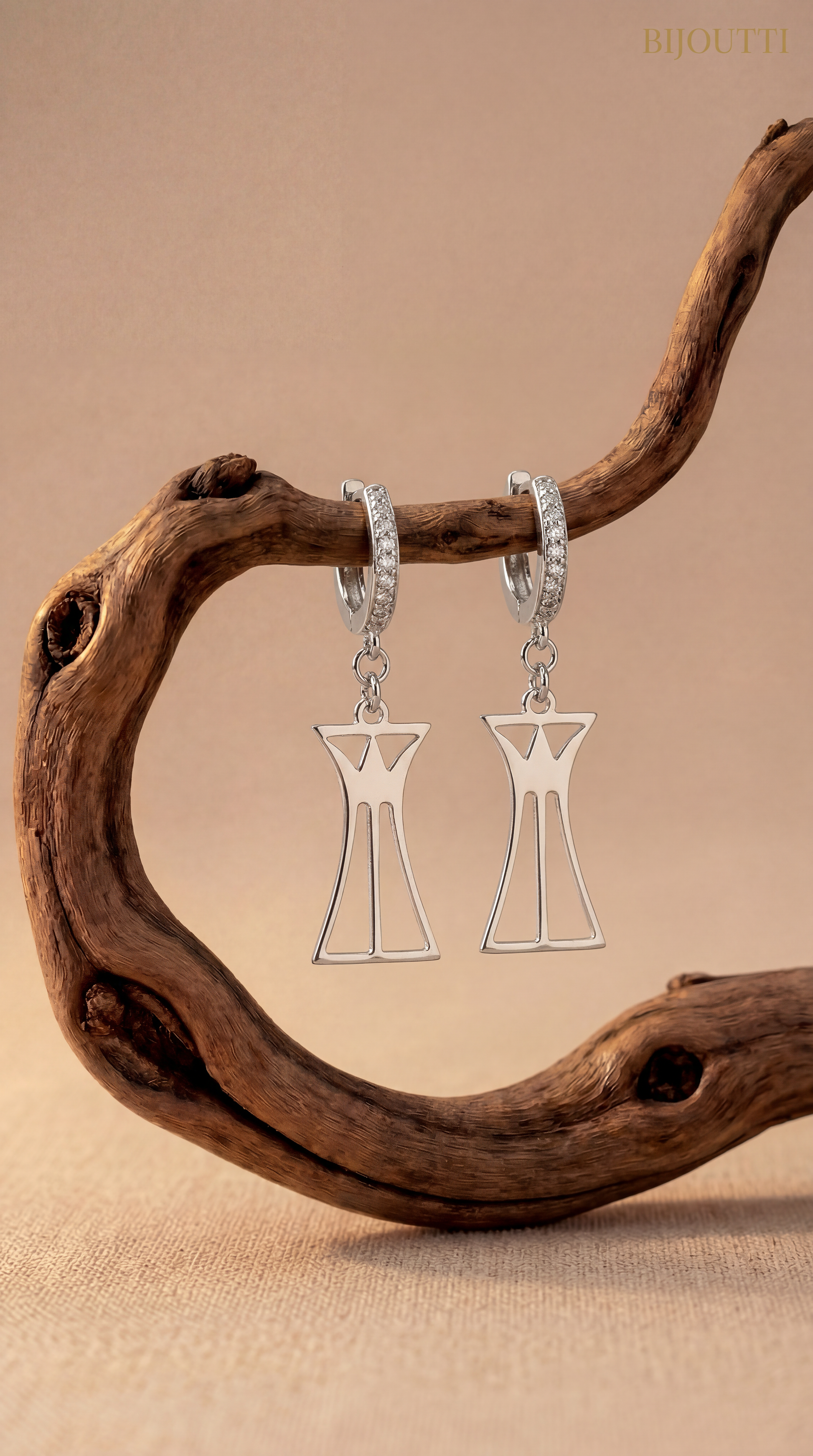 Silver lotus column earrings hanging from a branch with a beige background