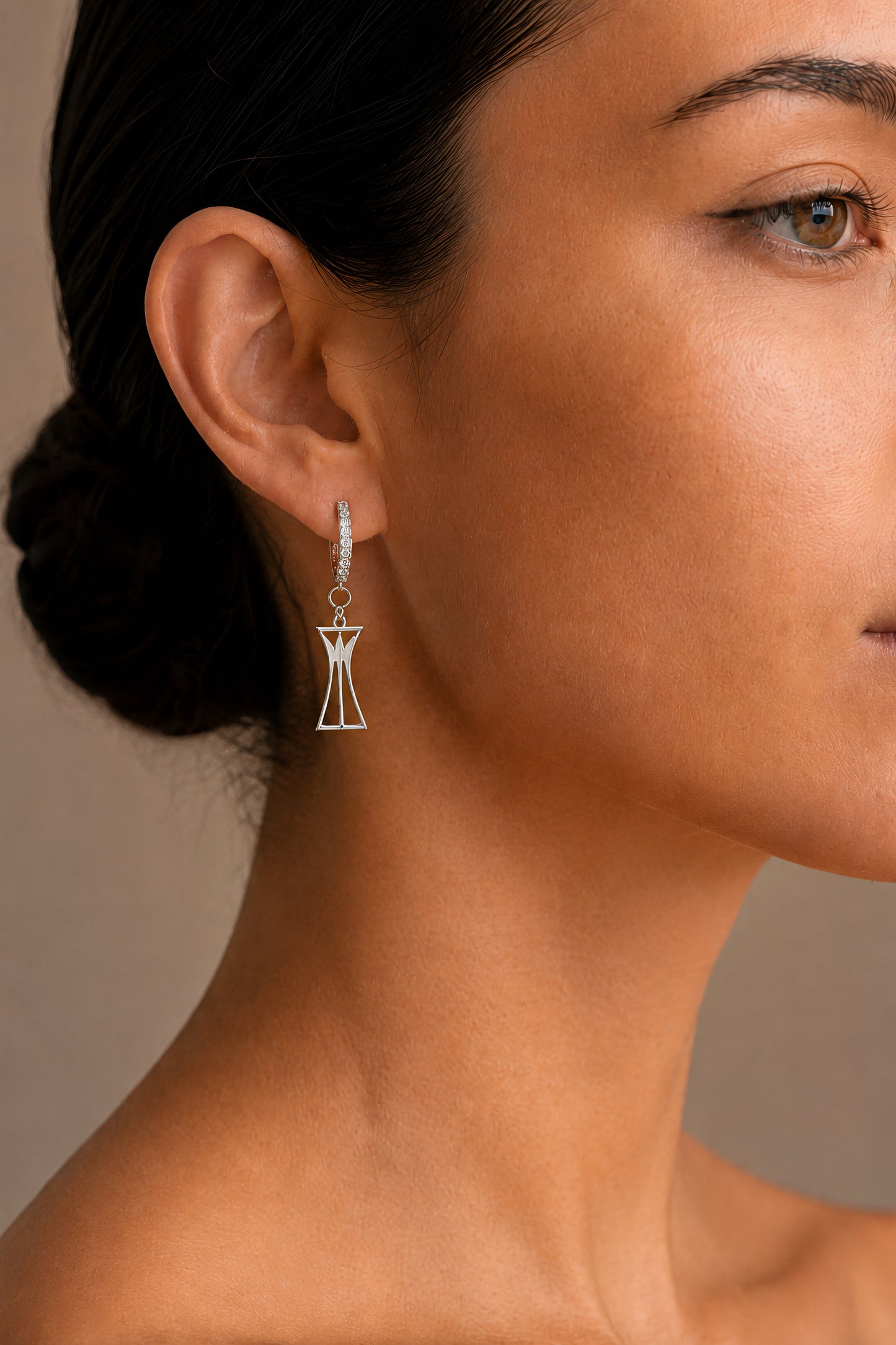 Close-up of a woman wearing a dangling lotus column earring with a neutral background