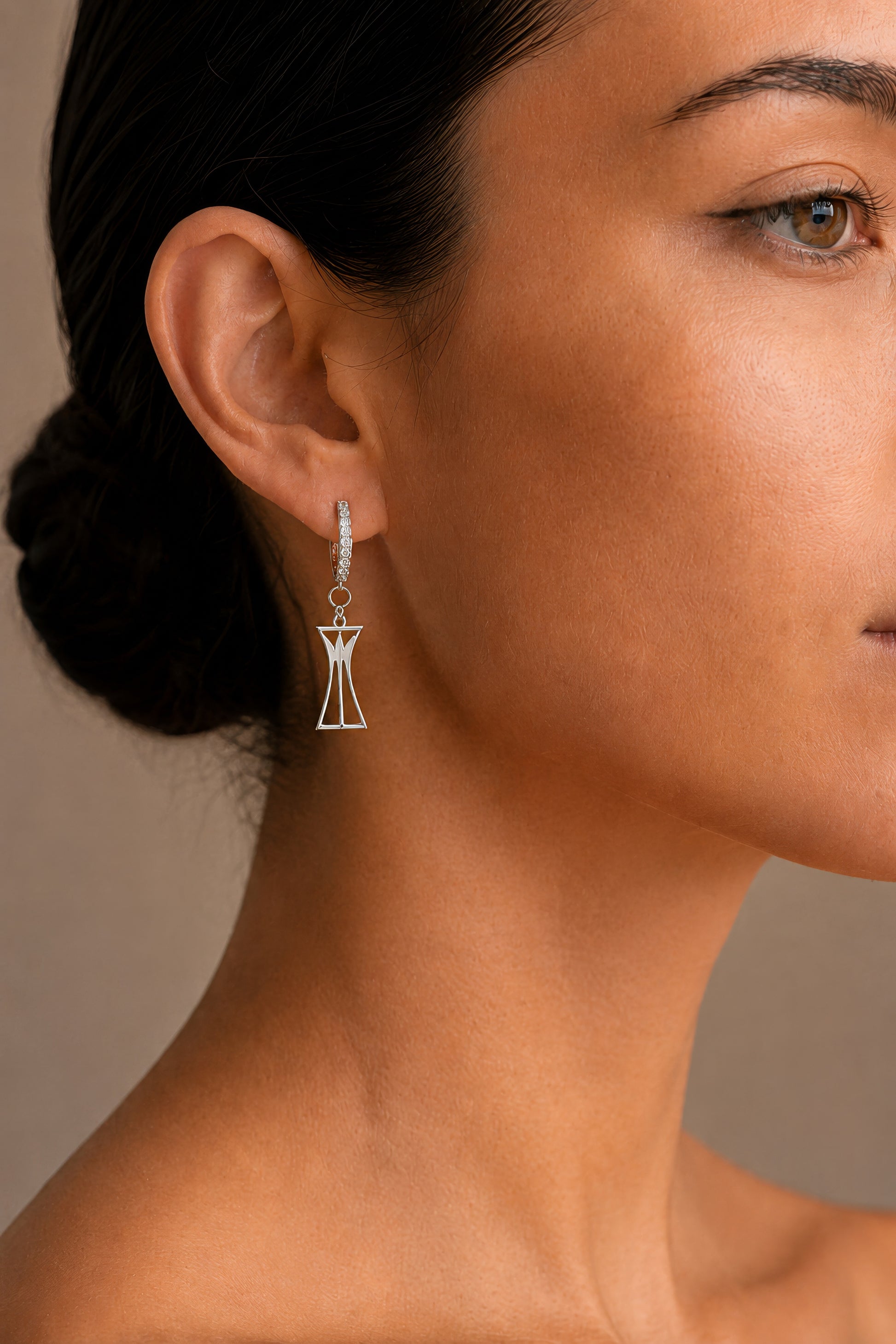 Close-up of a woman wearing a dangling lotus column earring with a neutral background