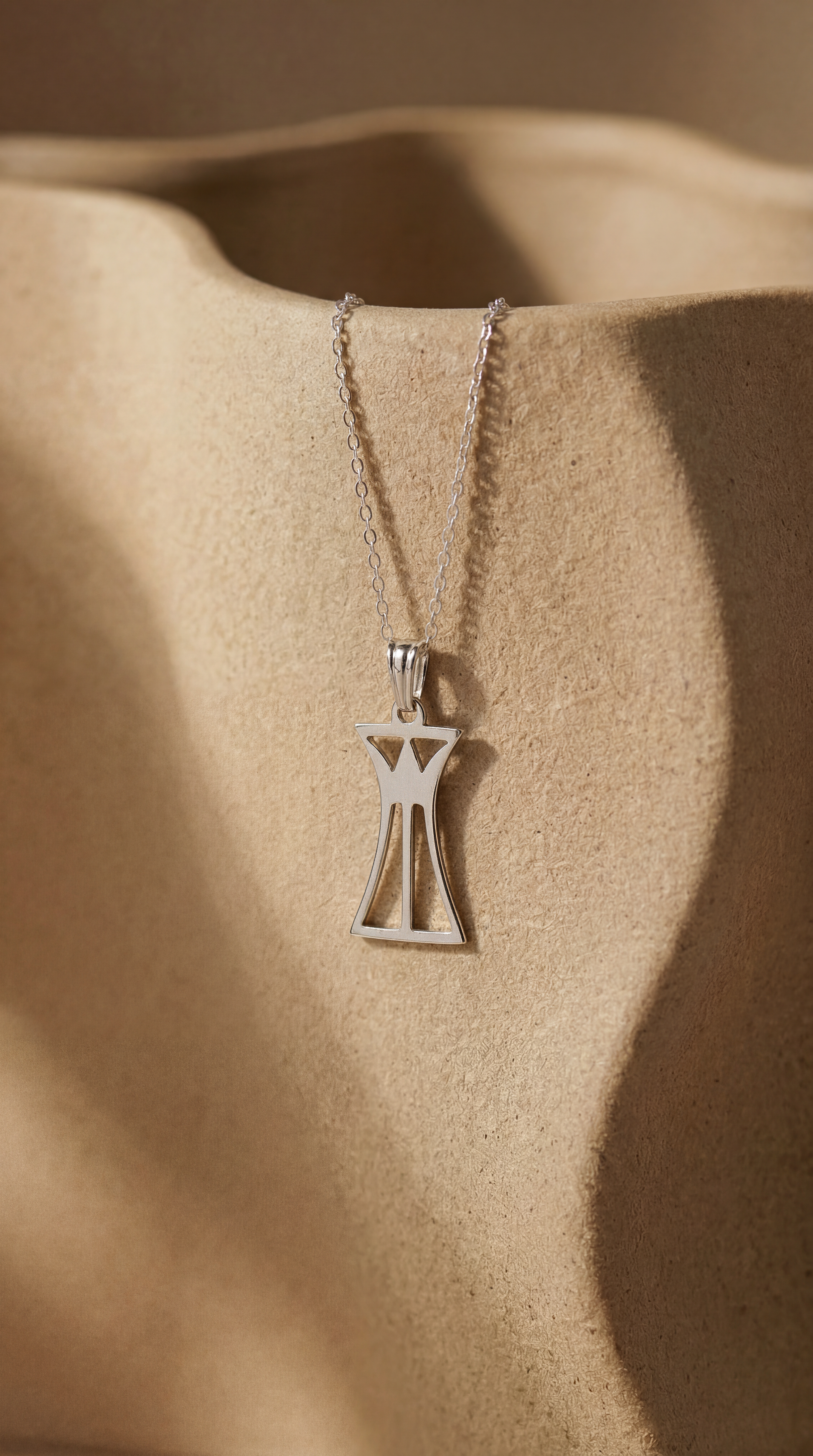 Silver necklace with a lotus column pendant on a beige fabric background