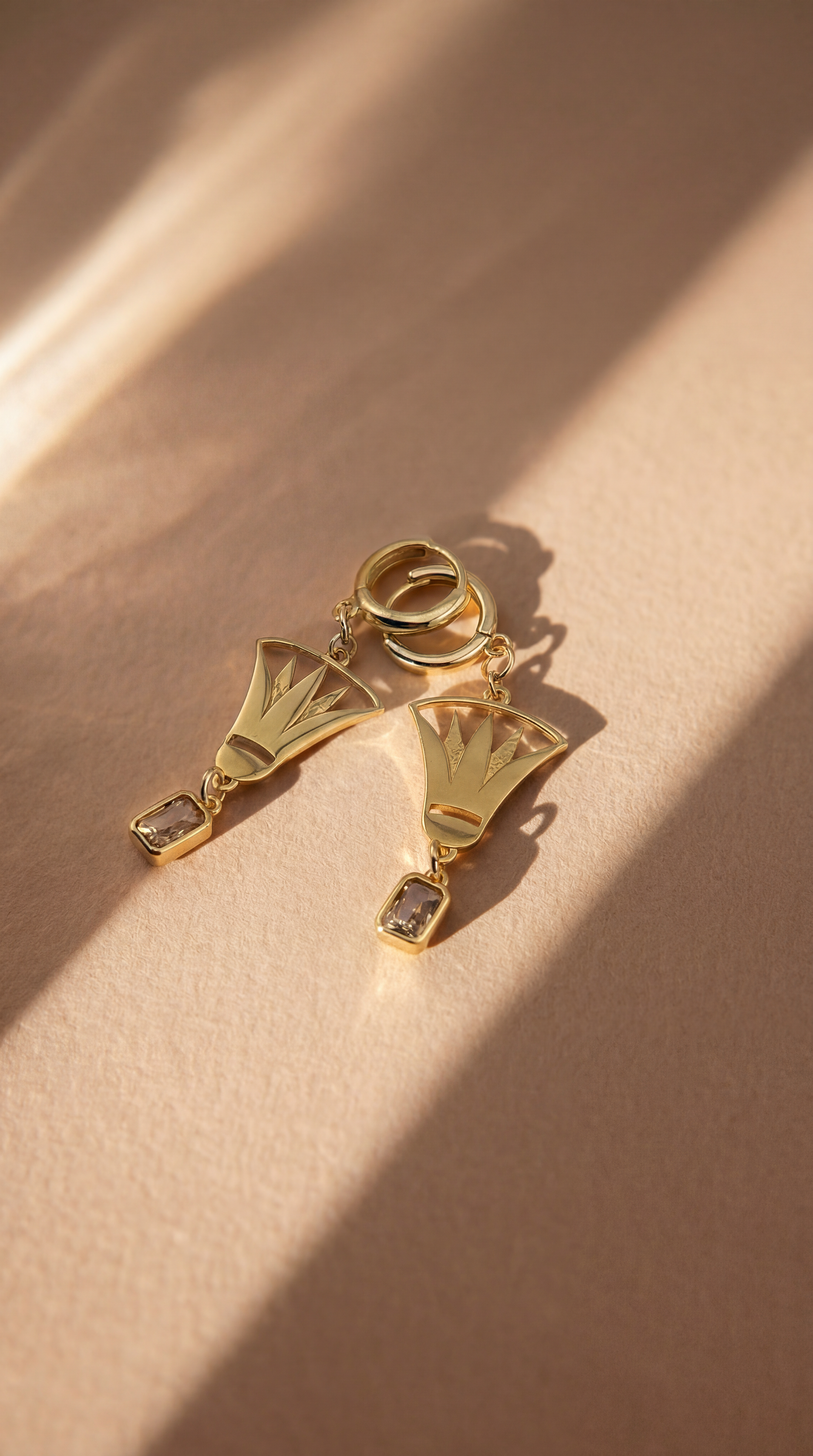 Gold earrings with fan lotus design on a beige background