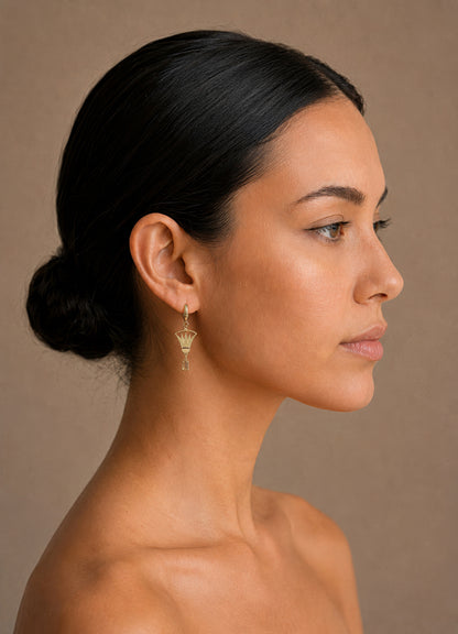 Woman with a side bun wearing gold lotus earrings against a beige background