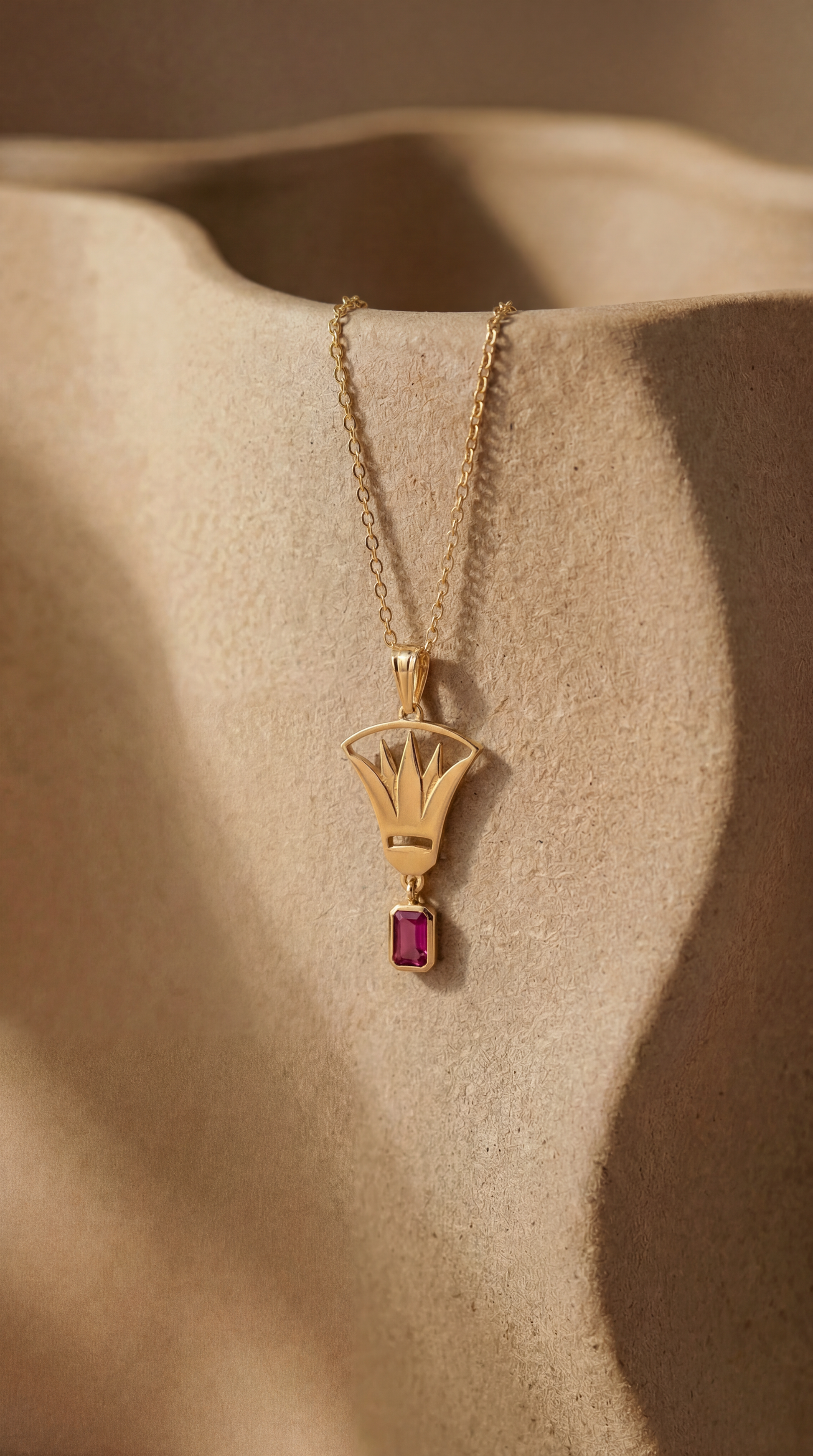 Gold necklace with lotus pendant and red zirconia stone on ceramic surface