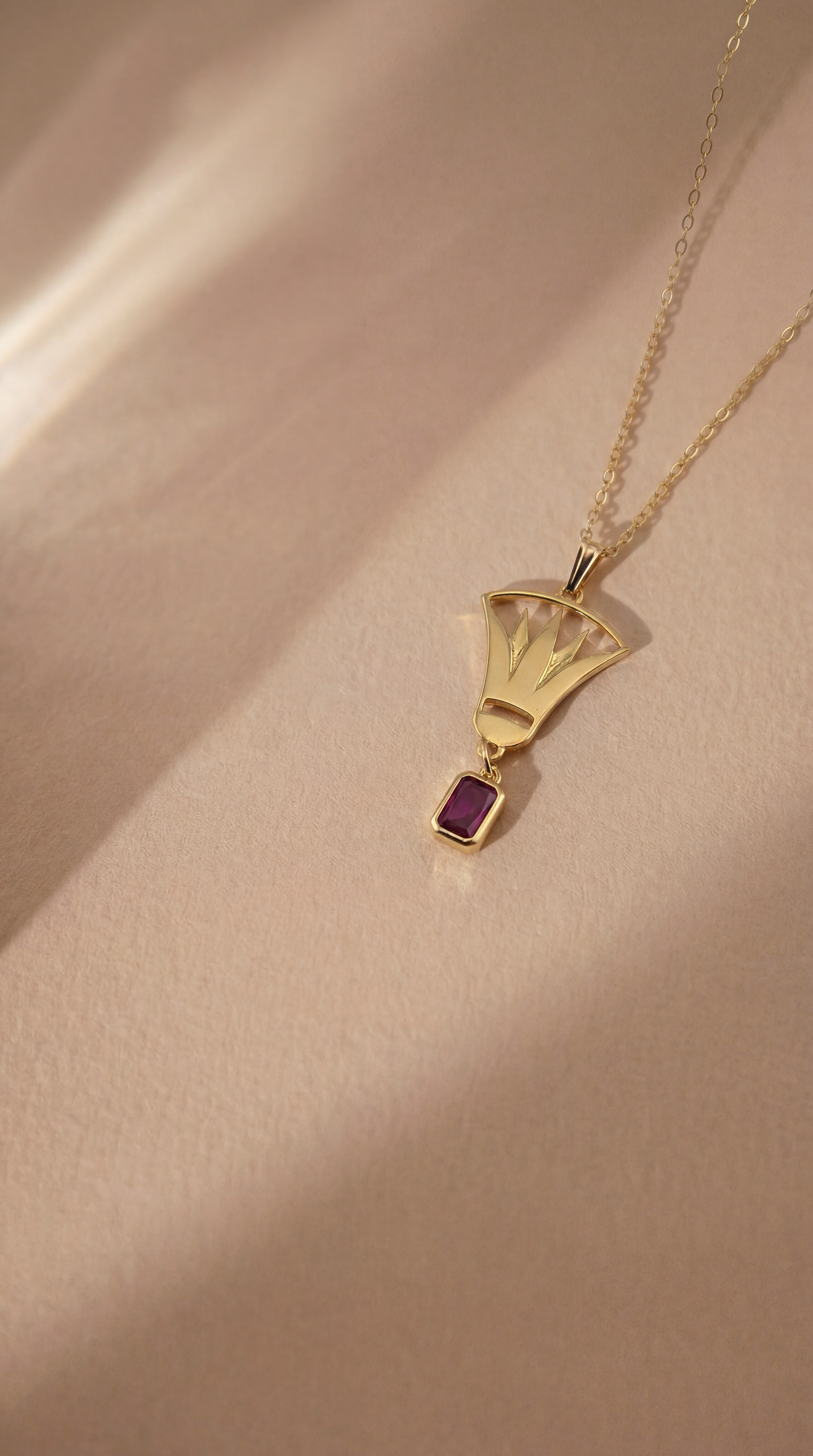 gold lotus necklace with red gemstone on beige background