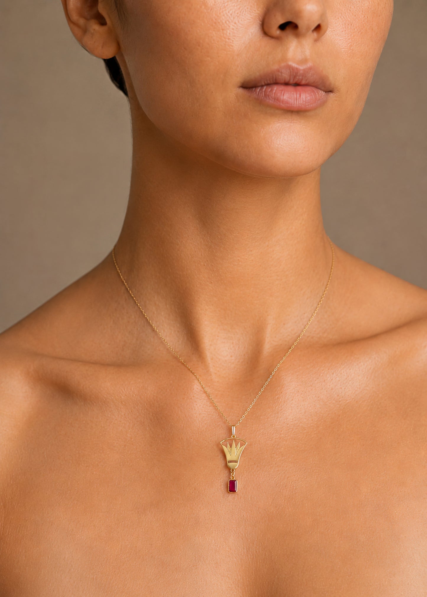 Close-up of a woman wearing a gold lotus necklace with a red gemstone pendant on a neutral background
