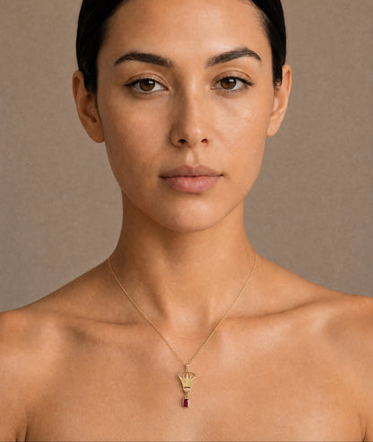 Woman wearing a gold lotus necklace with a red gemstone against a beige background