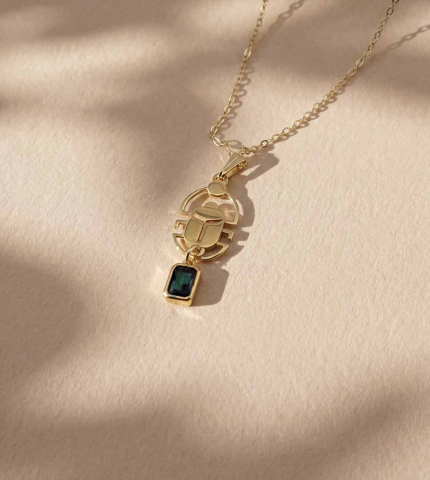 gold scarab necklace with a deep green gemstone on beige background