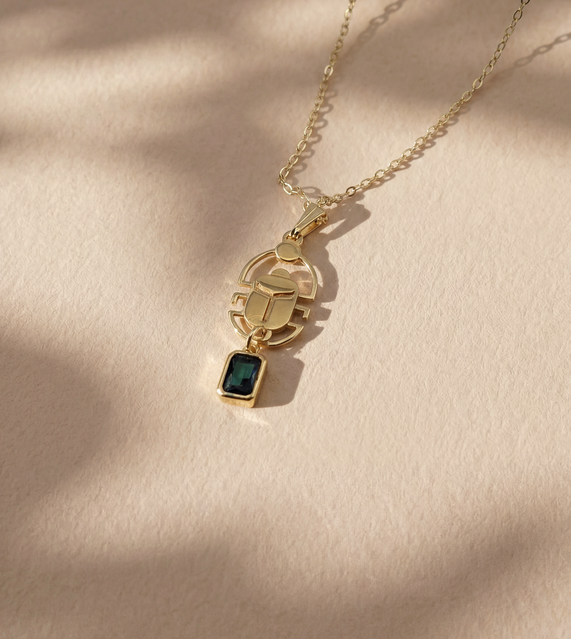 gold scarab necklace with a deep green gemstone on beige background