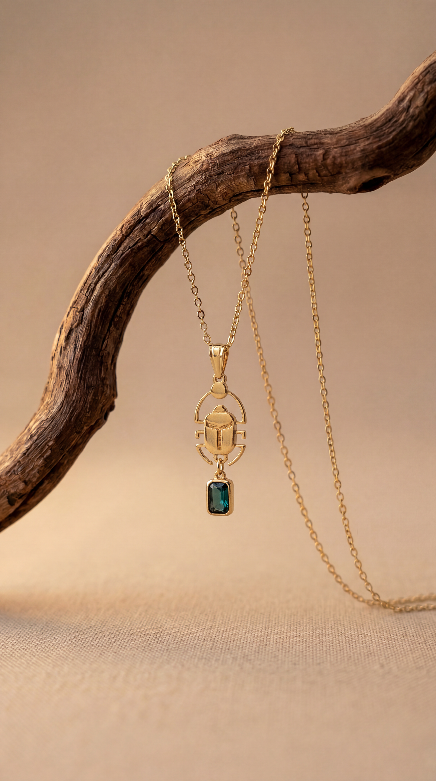 Gold necklace with a scarab pendant featuring a green gemstone on a wooden branch.