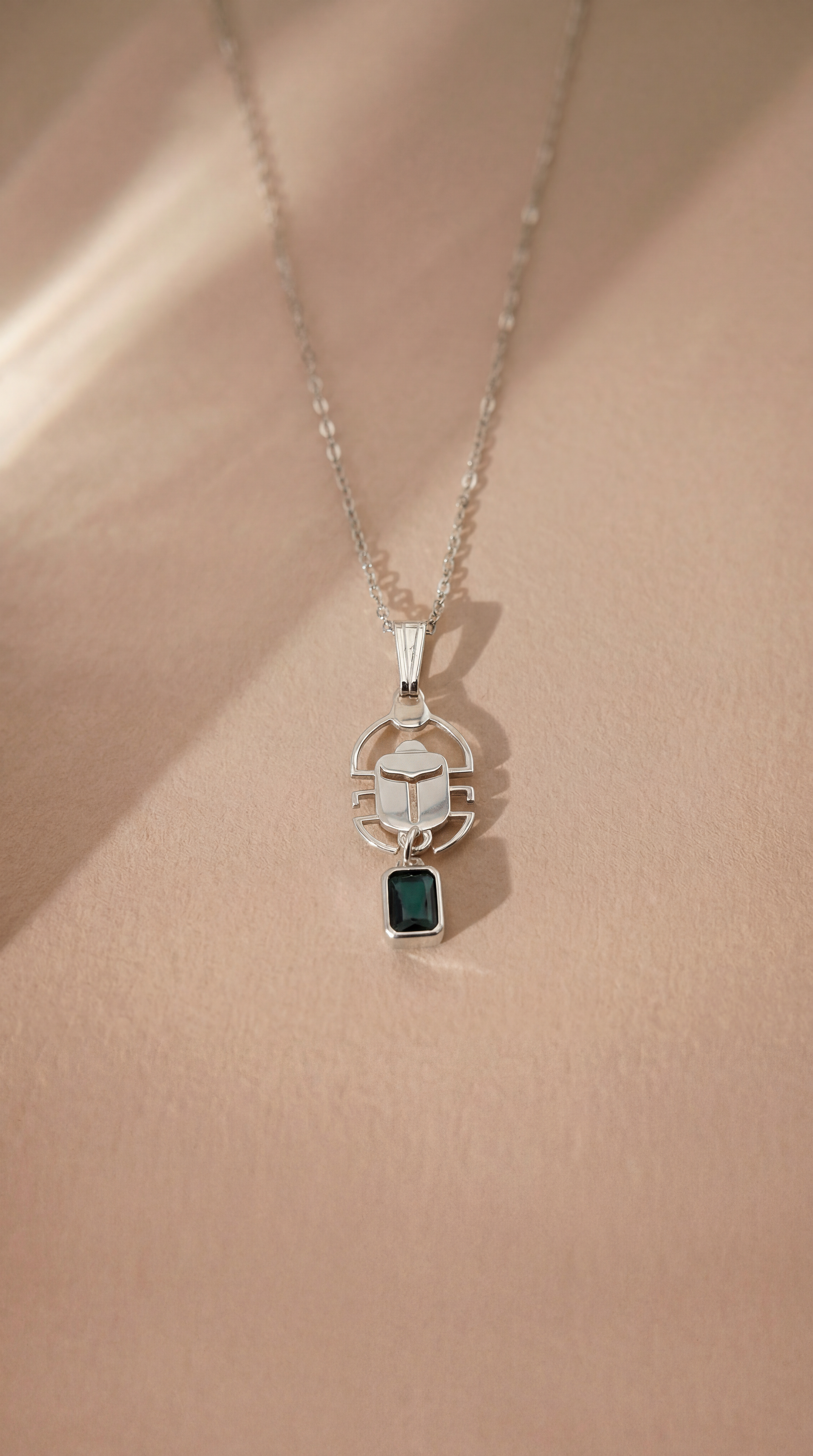 Silver scarab necklace with a green gemstone pendant on a beige background