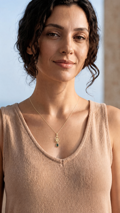Woman wearing a beige sleeveless top with a gold scarab necklace against a clear blue sky.