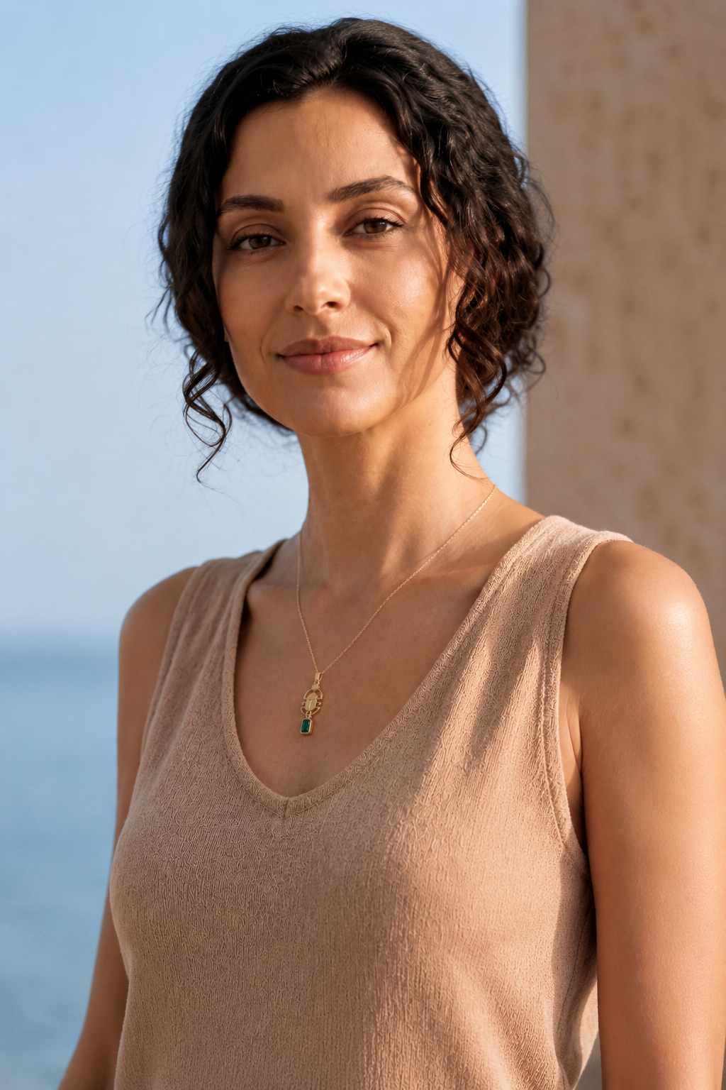 Woman wearing a beige tank top with a scarab necklace, standing against a clear blue sky.