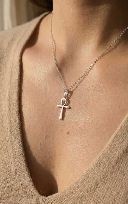 Silver ankh pendant necklace on a person wearing a beige top.