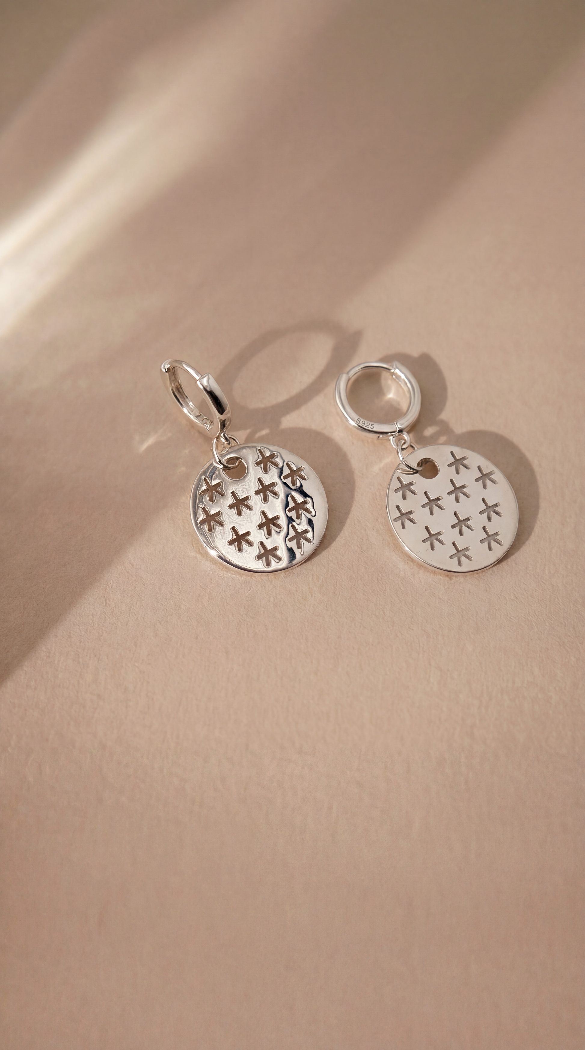 Silver earrings with star designs on a beige background