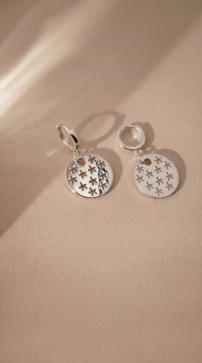 Silver earrings with star designs on a beige background