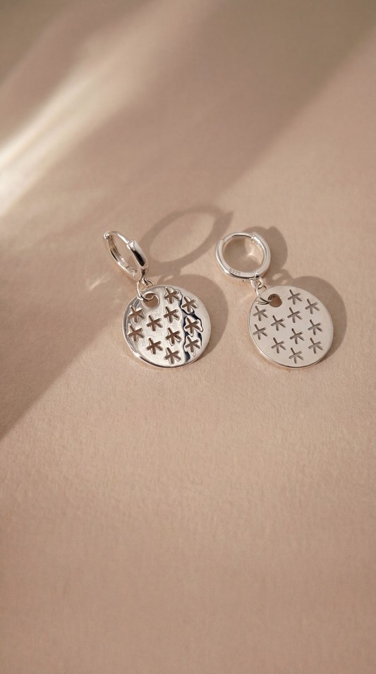 Silver earrings with star designs on a beige background